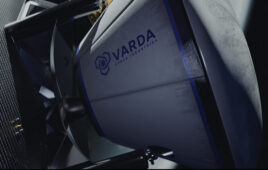 This is a screenshot from a Varda Space Industries promotional video showing a space capsule with the company's logo docking onto a satellite.